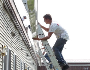 Two men on ladders holding an aluminum seamless gutter preparing to install on roof edge